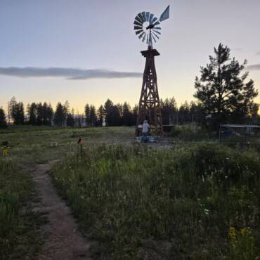 Mike and Laura beside an 8-foot Aermotor windmill and Amish hand pump on their Washington State homestead, tower by Big Sky Windmills.